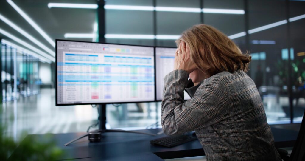 A woman sitting at a computer, using a spreadsheet, showing signs of anxiety.